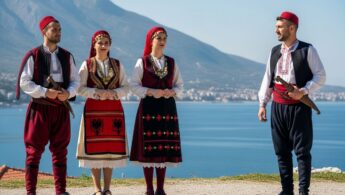 Trojica ľudí v tradičnom albánskom odeve s horským, pobrežným a mestským pozadím.